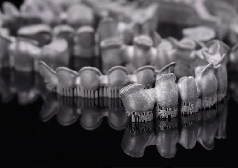 Impresora 3D de metal M-150 20 Conjunto de suministros dentales profesionales, incluyendo coronas y prótesis, dispuestos en una superficie reflectante, listos para su uso en procedimientos odontológicos.